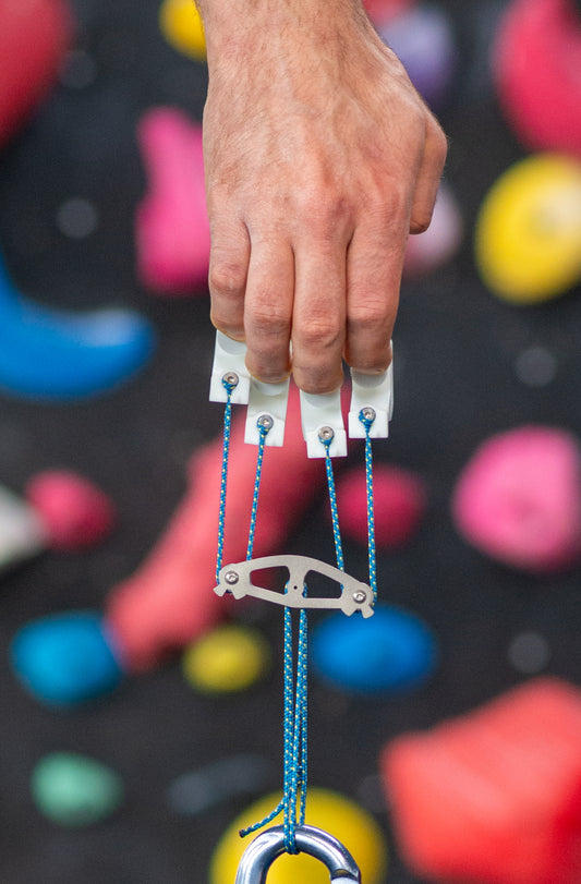 Hand holding the funky fingers finger trainer with a climbing wall in the background